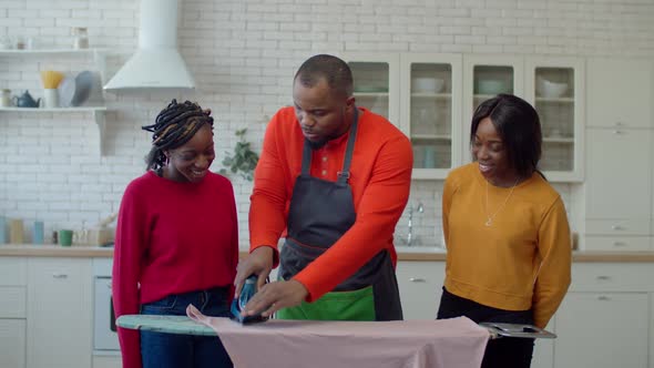 Caring Black Father Teaching Cute Teenage Daughters Ironing alt