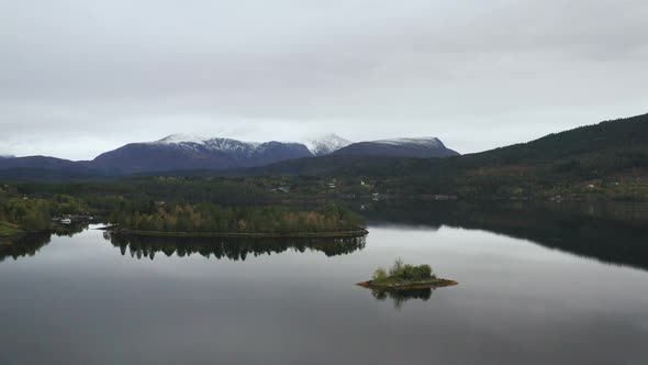 Calm Lake With Small Islands And Mountain Snowy View in The Background, Norway. - Aerial, pull in alt
