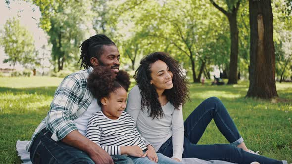 Lovely Black Family Has a Fan in the Park for a Picnic Sitting on a Blanket in the Middle of a Green alt