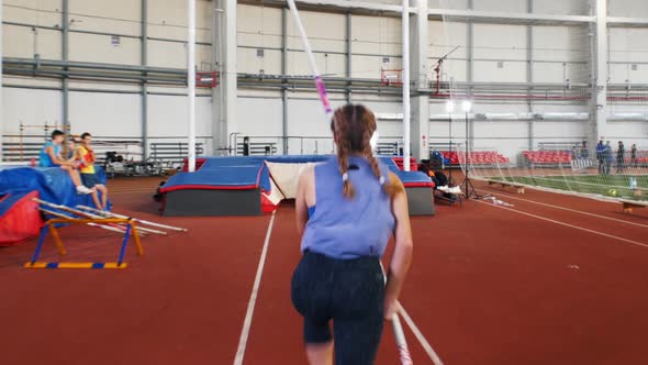 Pole Vaulting in the Indoors Stadium - Young Woman with Pigtails Jumping Over the Bar alt