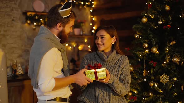 Young Man Gives New Year Present To His Girlfriend By the Christmas Tree alt