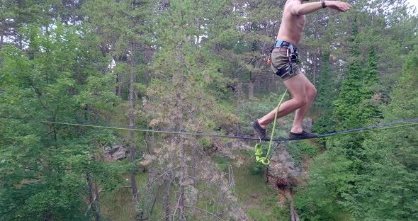A man tries to balance while slacklining on a tightrope in the mountains. alt