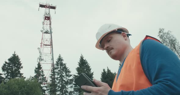 4G 5G Cellular Radio Tower Worker in Overalls and Helmet is Standing Next to It