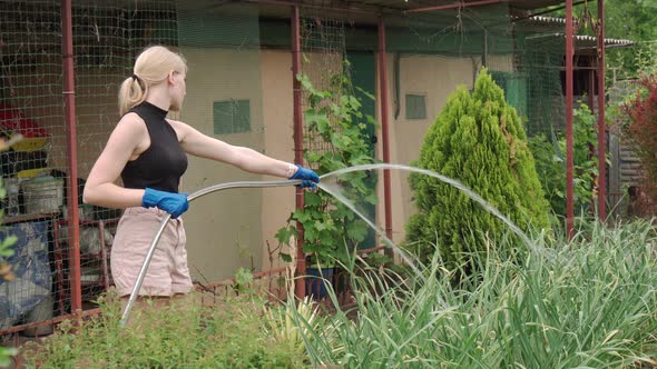 A Young Girl is Watering the Garden with a Garden Hose