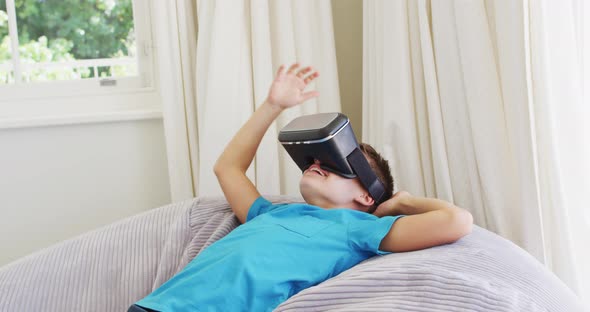 Caucasian boy wearing vr headset while lying on the bean bag at home alt