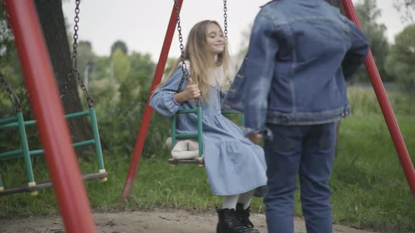 Unrecognizable Schoolboy Giving Bouquet of Flowers To Schoolgirl Swinging on Swings alt