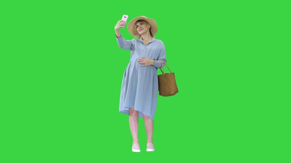 Happy Pregnant Woman in a Hat Using Her Smartphone Doing Selfie on a Green Screen, Chroma Key alt