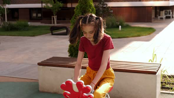 A Girl is Swinging on a Small Spring Swing on the Playground in the Courtyard alt