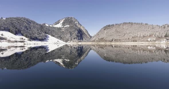 Movind drone shot over a mirroring lake in the swiss mountains. Mountain coverd with snow. alt