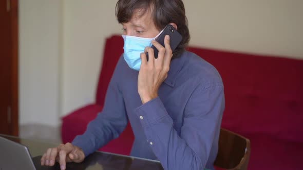 A Young Man Wearing a Face Mask Works From Home During Coronavirus Self-isolation. He Talks on a alt