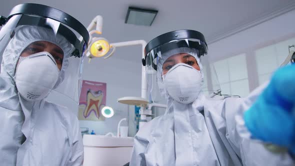 Dental Team in Coverall Leaning Over Patient to Work on Patient Gums alt