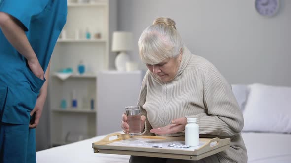 Elderly Female Patient Spilling Water on Tray While Taking Pills, Bad Service alt