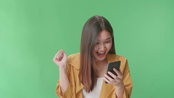 Young Asian Woman Use Mobile Phone, Surprised And Saying Wow In The Green Screen Studio alt