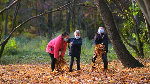Small children in medical masks throw fallen yellow leaves in the Park on an autumn day