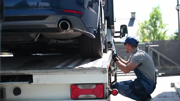 Truck Driver Securing Car On Flatbed Trailer.  alt