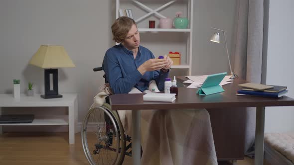 Portrait of Sad Disabled Man in Wheelchair with Vitamins at Home Indoors alt