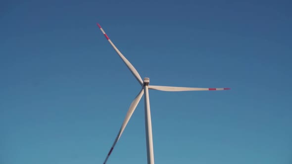 Closeup of a Working Windmill with Three Red Blades Against a Cloudless Blue Sky