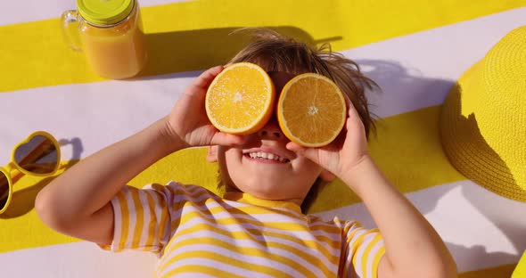 Happy child holding halves of orange fruit like a sunglasses. Slow motion
