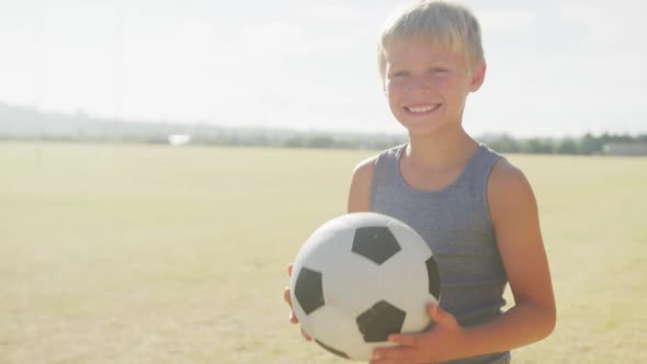 Video of happy caucasian boy holding ball on sports field alt
