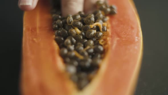 Close up of female fingers diving into the seeds of papaya cut in half alt