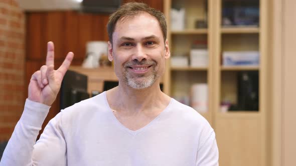 Victory Sign By Middle Age Man in Office alt