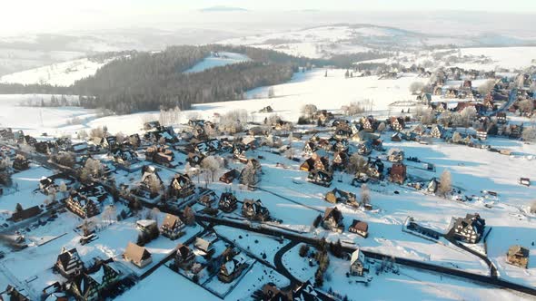 Drone View of Cottages and Houses on Snowy Terrain in Mountains with Bright Sunshine