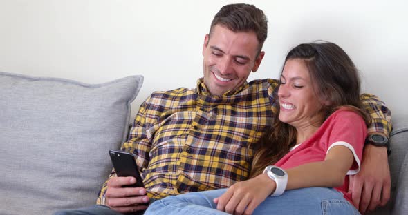 Cute couple using mobile phone in living room at home 