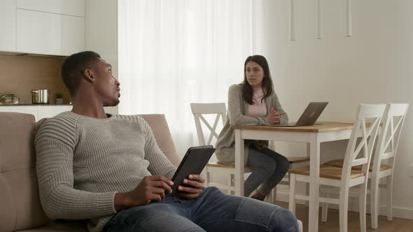 Young Adult Couple Chilling at Home Browsing the Web on a Tablet and Working on a Laptop at Home alt