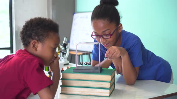 Two African American Kids Using Magnifying Glass and Pulling Cradles Ball Swing in Science Classroom alt