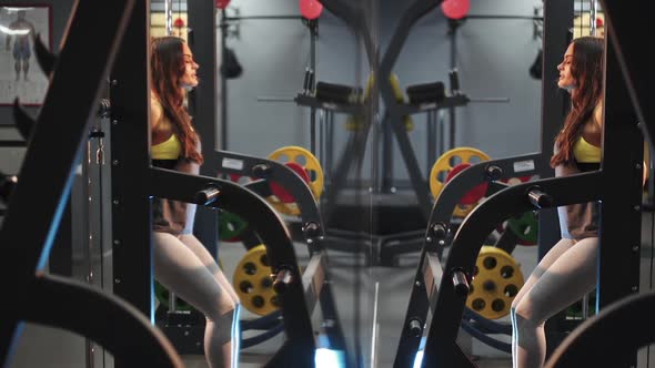 Beautiful girl in the gym is squatting with a barbell. Strength exercises for the feet. alt