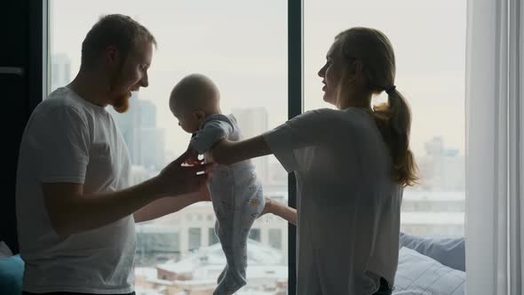 parents play with their baby at a large window overlooking the city