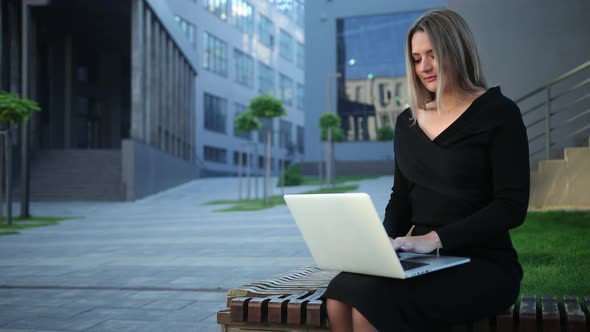 Attentive woman working on a laptop sitting bench in the street. Businesswoman alt
