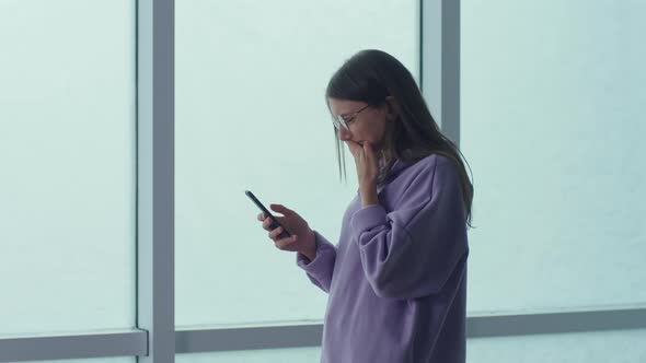 Stressed Woman Standing With Phone in Hands Looking at Phone Screen alt
