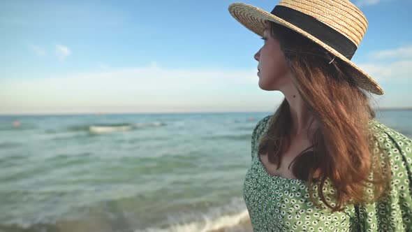 Romantic Portrait of Attractive Caucasian Young Woman in Green Dress and Straw Hat on the Seashore alt