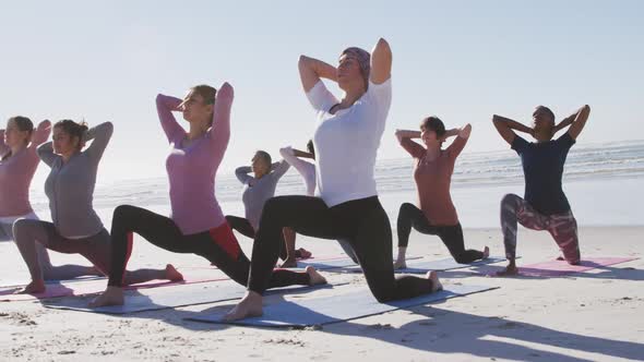 Multi-ethnic group of women doing yoga position on the beach and blue sky background alt