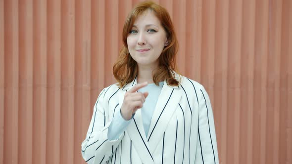 Portrait of Cheerful Woman Shushing Touching Lips with Fingers and Smiling Outdoors alt