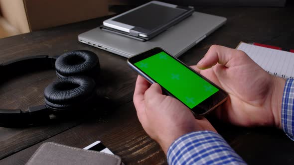 Hands of Man Using Smartphone with Green Screen on Wood Table alt