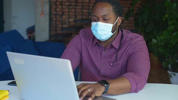 Concentrated AfricanAmerican Male Employee Wearing Medical Mask Using Laptop alt