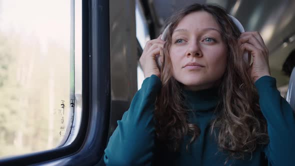 Woman Travelling By Electric Train Puts on White Headphones alt