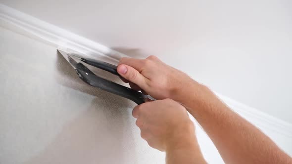 Man Cuts Wallpaper Near Ceiling Moldings Using Box Cutter and Putty Blade