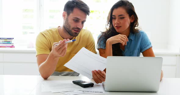Worried couple calculating their bills with laptop in the kitchen alt