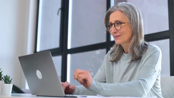 Stylish Mature Business Woman Wearing Eyeglasses is Using Laptop Sitting at the Desk