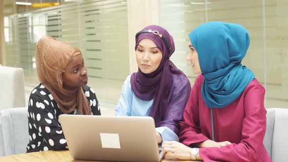 Group of Multi-ethnic Muslim Business Ladies Sit in Cafe and Making Online Purchases Using a Laptop.