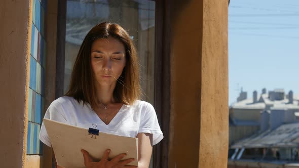 Dark-Haired Girl Painting Outside On Balcony In The Downtown. alt