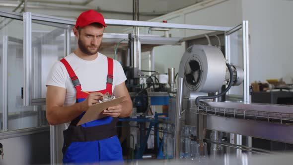 Young Factory Man in Uniform Making Notes on Clipboard at Water Production Factory