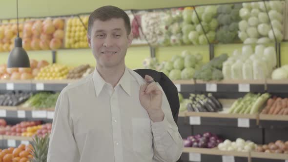 Portrait of Cheerful Young Caucasian Brunette Man with Brown Eyes Posing in Grocery. Happy Adult Guy alt