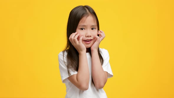 Funny Little Japanese Girl Posing Touching Face Over Yellow Background alt