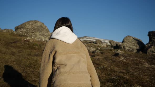 A Girl in a Beige Jacket and Hooded Jacket Runs Up Walking High in the Mountains alt