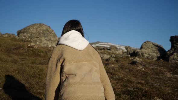 A Girl in a Beige Jacket and Hooded Jacket Runs Up Walking High in the Mountains