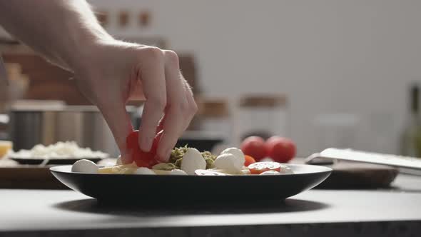 Slow Motion Orbit Shot of Man Add Cherry Tomatoes to Pesto Penne on Black Plate alt